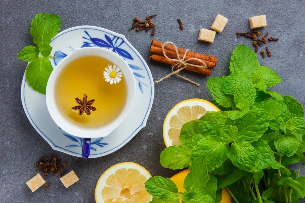 Set of mint leaves, lemon, sugar, dry cinnamon and a cup of chamomile tea on a gray background. top view.