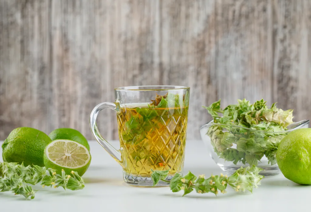 Herbal tea with herbs, limes in a glass cup on white and grungy background, side view.