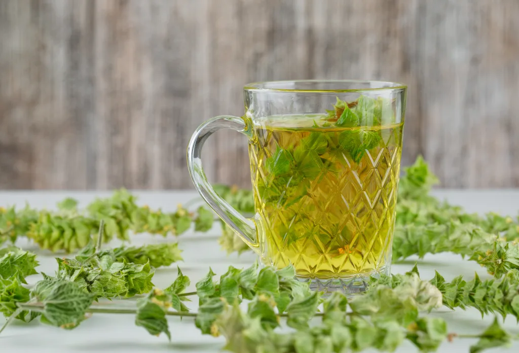 Herbal tea with leaves in a glass cup on white and grungy background, side view.